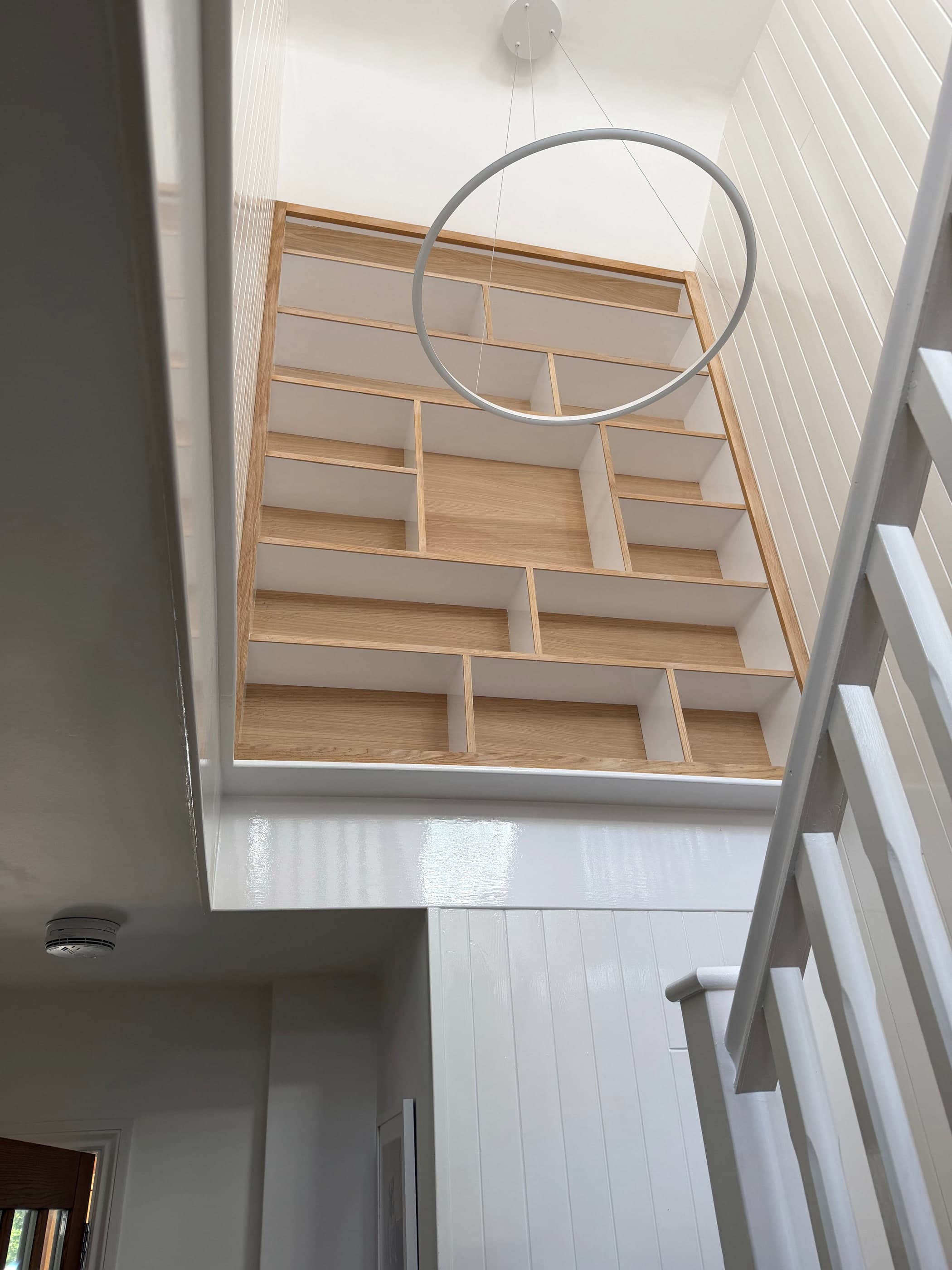 Oak shelving unit viewed from the foot of the stairs, showing its scale within the stairwell void