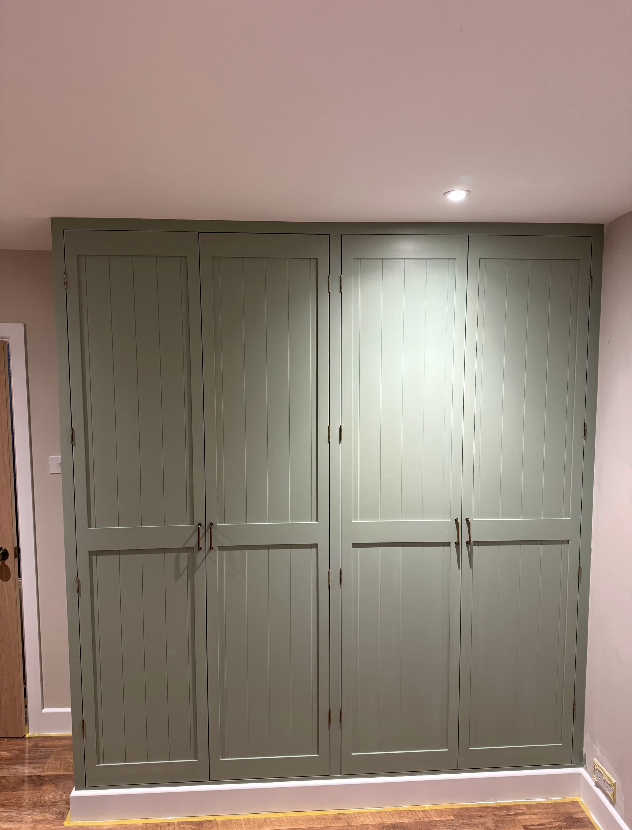 Bespoke four-door fitted wardrobe painted in sage green, built floor to ceiling in a Surrey bedroom